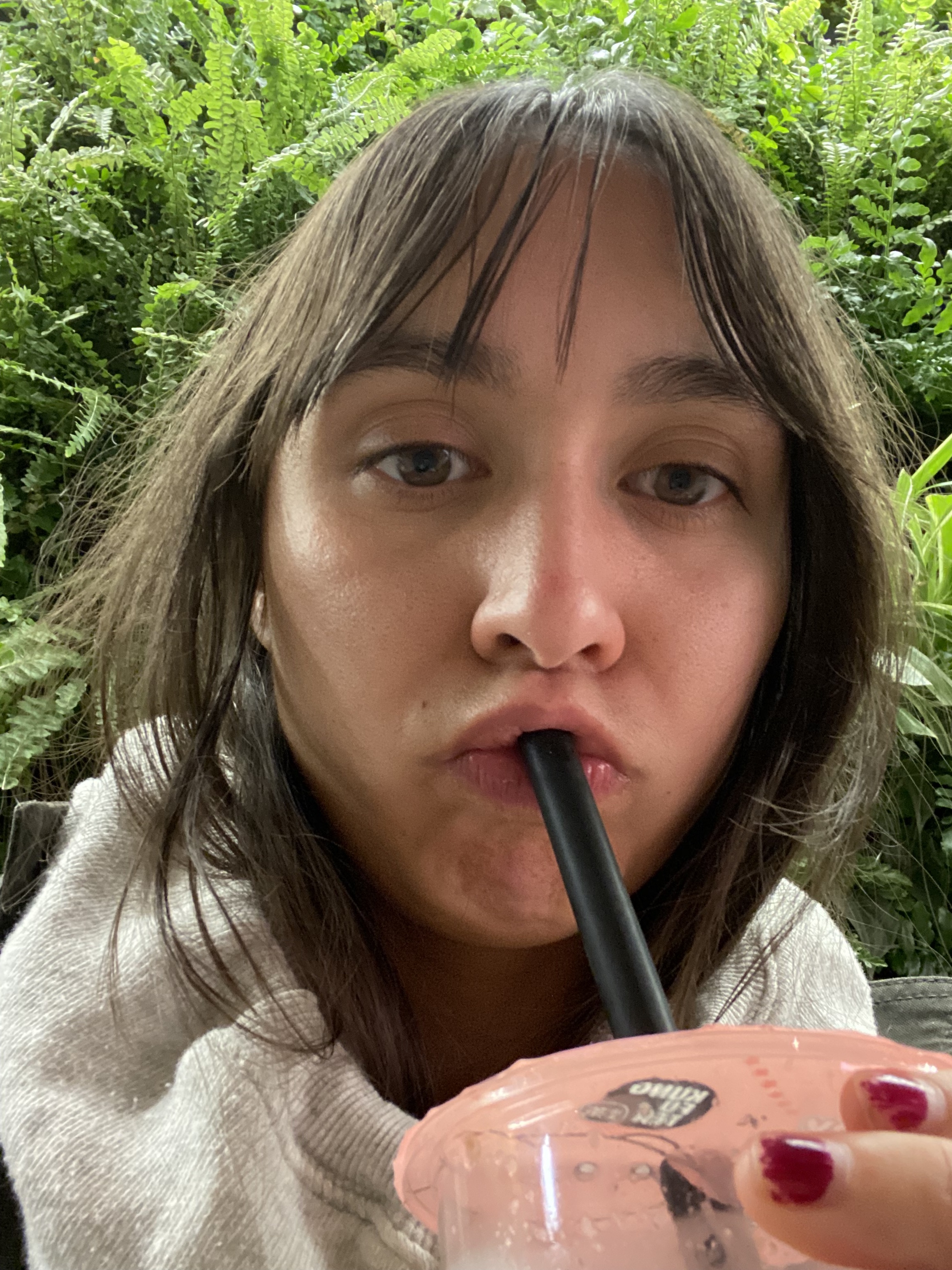 Closeup front camera photo of me drinking boba in front of a wall of greenery at the Palo Alto Apple Store