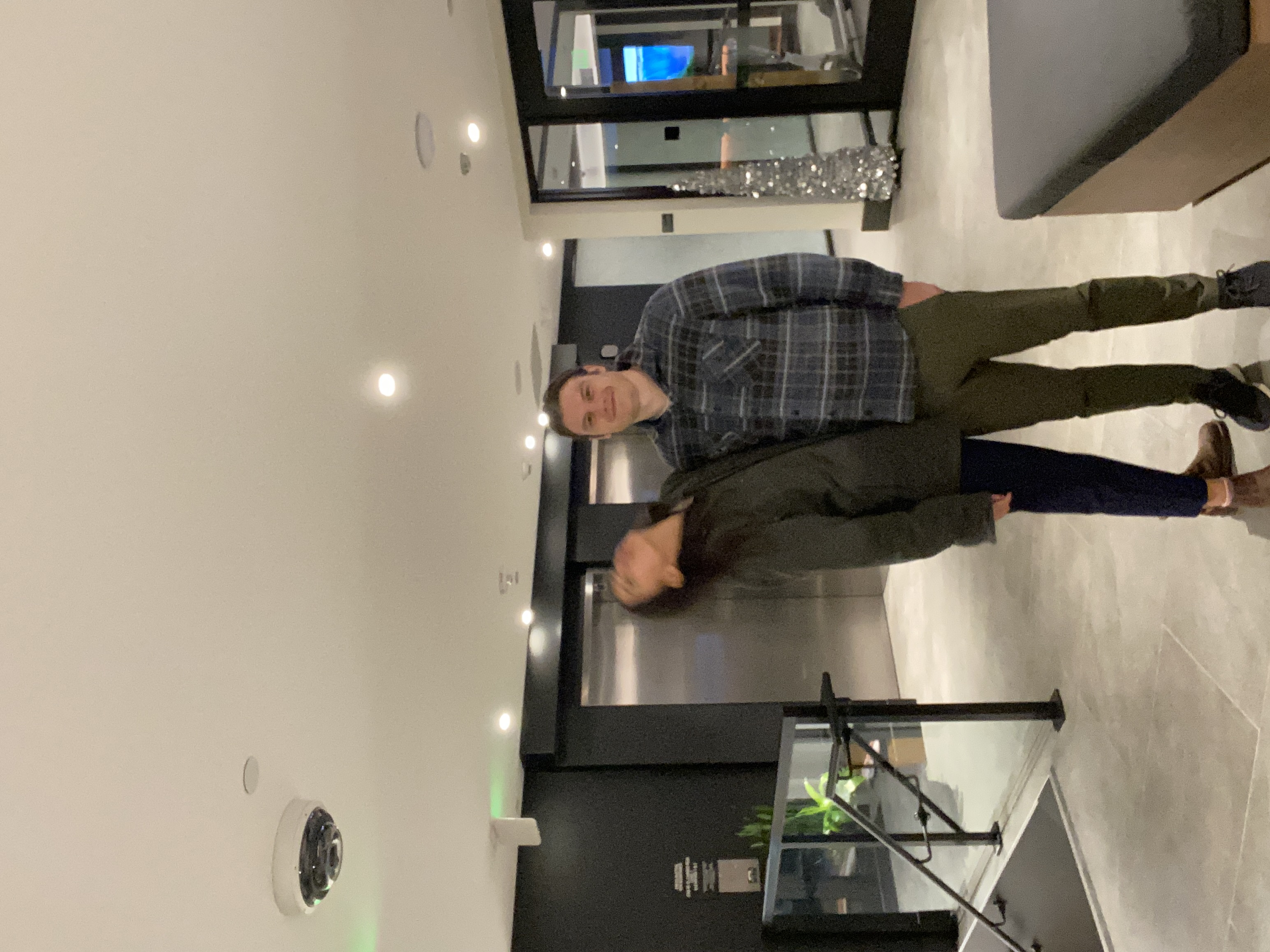 Fitpic-style photo taken in the lobby of an apartment building. Marika is blurry from moving while the photo was taken and Travis looks nice.